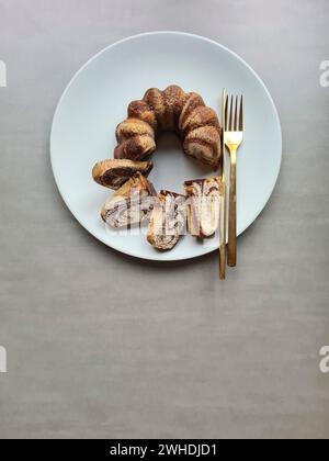 Pieces of cut marble cake lie on the light gray plate next to the golden cutlery Stock Photo