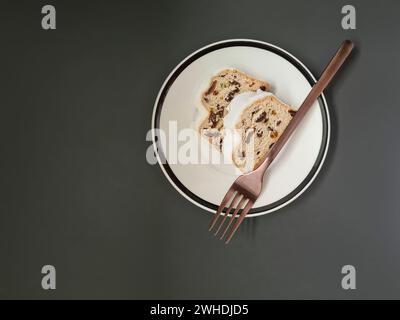 Two slices of Christmas cake with white powdered sugar on a white plate with a black rim and a copper-colored fork Stock Photo