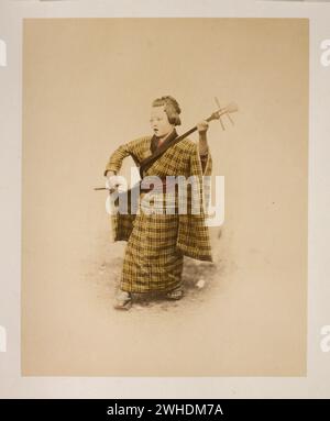 Photograph shows a young woman, full-length, standing, facing left, playing a shamisen and singing. This is a detail of a photograph taken by Felice Beato showing three street musicians....Japan  Hand-coloured with watercolour Photographic Print circa 1870s Stock Photo
