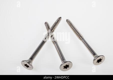 Three Torx chipboard screws with countersunk head, stainless steel, white background, Stock Photo