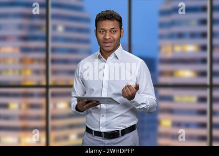 Young Indian business man giving a presentation using digital tablet. City night background inside office. Stock Photo