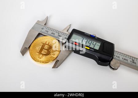 Electronic caliper measures the diameter of a Bitcoin coin, white background, Stock Photo