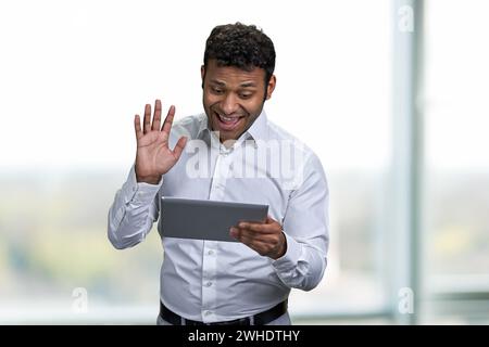Cheerful african-american businessman making video call with digital tablet. Handsome man waving with hand while talking via internet. Stock Photo