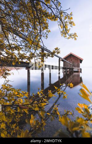 Boathouse with spring foliage framing on the Ammersee. Long exposure with reflection in the water Stock Photo