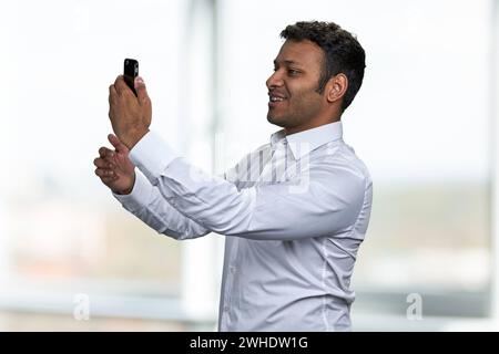 Handsome Indian man taking photo with mobile phone. Young man having video call with smartphone. Stock Photo