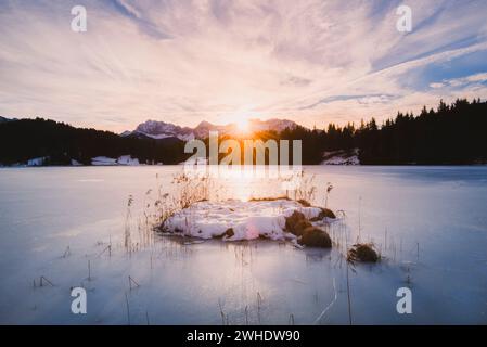 Winter sunrise over the frozen Geroldsee (Wagenbrüchsee) with a view of a forest silhouette and the Karwendel mountains, Mittenwald, Garmisch-Partenkirchen, Karwendel, Upper Bavaria, Bavaria, Germany Stock Photo