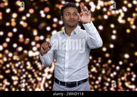 Young attractive indian businessman working on invisible interface. Festive bokeh lights in the background. Stock Photo
