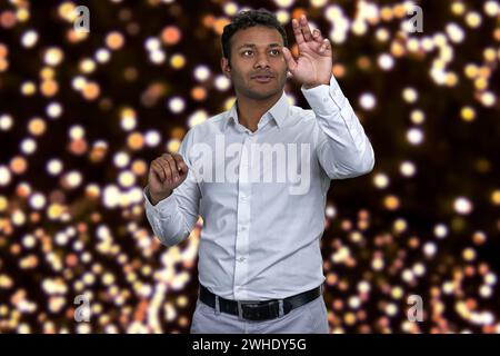 Young attractive indian businessman working on invisible interface. Festive bokeh lights in the background. Stock Photo