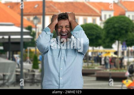Desperate young man holding head with hands standing outdoors. People, depression and problems concept. Stock Photo