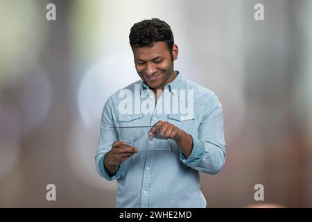Smiling young man using transparent digital tablet. Abstract bokeh background. Stock Photo