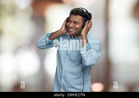 Cheerful young indian man listening music with headphones. Interior blur background. People, leisure and fun concept. Stock Photo