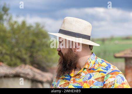 Young bearded man in fedora hat standing smiling happily. Close-up portrait of a bearded young man wearing casual clothes looking at the camera with a Stock Photo