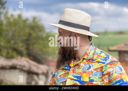 Young bearded man in fedora hat standing smiling happily. Close-up portrait of a bearded young man wearing casual clothes looking at the camera with a Stock Photo