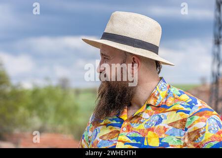 Young bearded man in fedora hat standing smiling happily. Close-up portrait of a bearded young man wearing casual clothes looking at the camera with a Stock Photo
