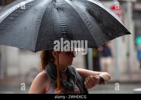 "10.07.2019, Ireland, County Dublin, Dublin - Young woman with umbrella looking at the clock, rainy day in the city (city center). 00A190710D049CAROEX Stock Photo