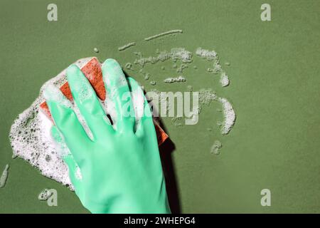 Hand in green rubber glove scrubbing with a sponge and foam, close-up shot Stock Photo
