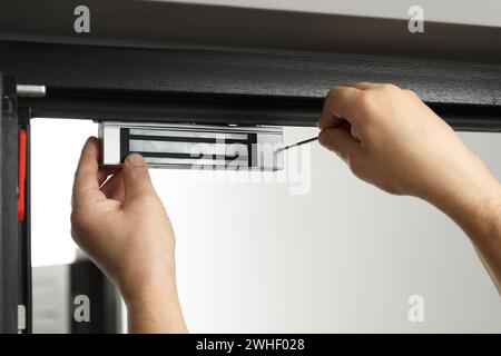 Man with screwdriver installing electromagnetic door lock indoors, closeup. Home security Stock Photo