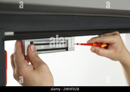 Man with screwdriver installing electromagnetic door lock indoors, closeup. Home security Stock Photo