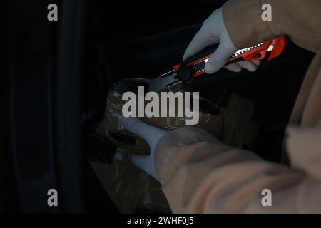 Man opening package of narcotics with stationery knife on dark background, closeup. Space for text Stock Photo