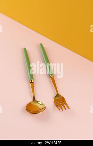 Golden Spoon and Fork with Green Olive Handle on Pink and Yellow Background Stock Photo