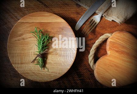 Vintage silverware, cutting board, plate, rosemary on rustic wooden background. Top view of kitchen setting table Stock Photo