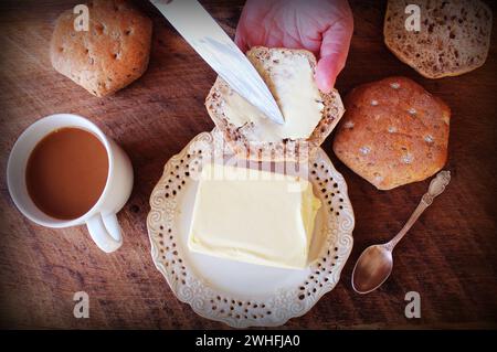Women hand with a knife spreads butter on bread .Breakfast background Stock Photo