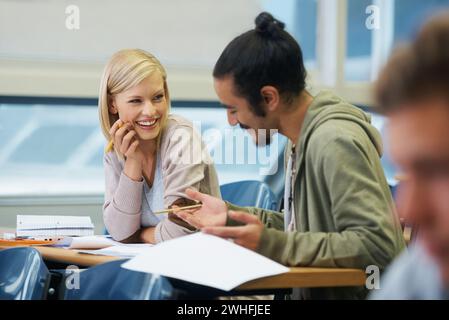Conversation, college and students in classroom for studying with text book for test or exam. Discussion, writing and young friends work on university Stock Photo