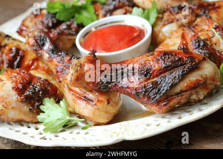 Grilled chicken legs on wooden table served on white plate with coriander Stock Photo