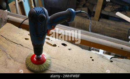 blue electric drill standing on a round mounted brush with metal bristles on a wooden surface in a craftsman's workshop, hand tools for woodworking Stock Photo