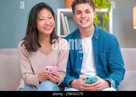 Portrait of young smiling multiethnic couple using smartphone technology.Indoors Stock Photo