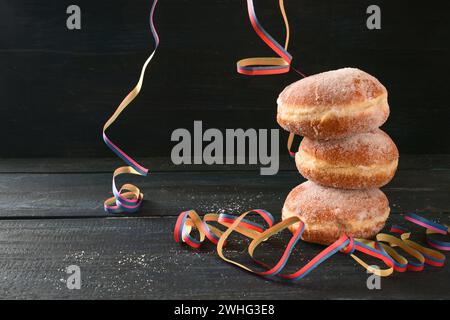 Stacked Berliner doughnuts or Krapfen and some party streamers against a dark rustic background, often served on New Year and ca Stock Photo