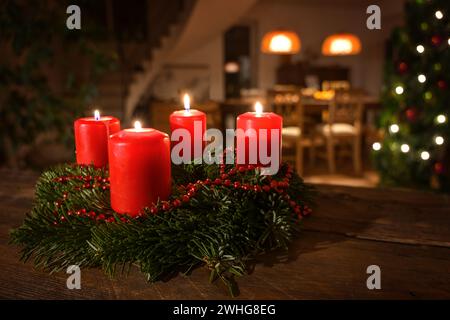 Decorated Advent wreath from fir branches with red burning candles on a dark wooden table, living room with Christmas tree blurr Stock Photo