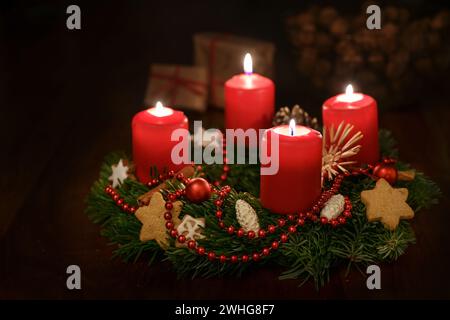 Advent wreath from fir branches with red lit candles and Christmas decoration, some gifts blurred in the dark background, copy s Stock Photo