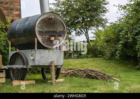 Homemade mobile pizza oven from an old metal barrel on a recycled chassis in a garden, fire in the combustion chamber and firewo Stock Photo