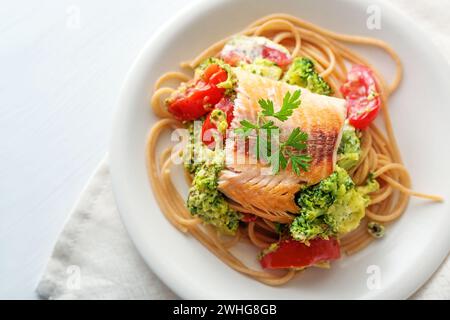 Wild salmon fillet on whole grain spaghetti with broccoli, tomatoes and parsley garnish, healthy meal on a white plate, copy pac Stock Photo