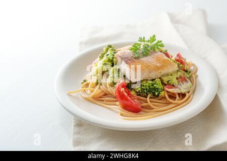 Wild salmon fillet on whole grain spaghetti with broccoli, tomatoes and parsley garnish, healthy seafood meal on a white plate, Stock Photo