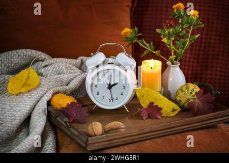 Fall back in autumn after daylight saving time, white alarm clock on a wooden tray with candle and warm colored fall decoration Stock Photo