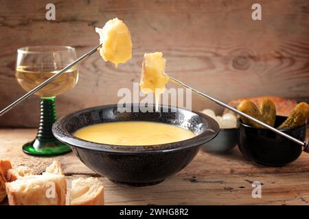 Swiss fondue from melted cheese with bread on long forks, pickles and wine on rustic wooden planks, copy space, selected focus Stock Photo