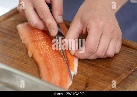 Hands of a cook remove the belly flap with bones of a fresh raw char fish with a filleting knife on a cutting board, selected fo Stock Photo