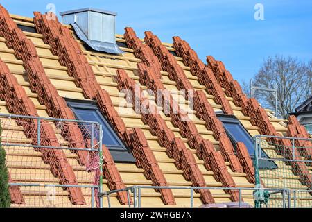 Clay roof tiles stacked on the roof of a residential house in preparation for roofing on a construction site, blue sky Stock Photo