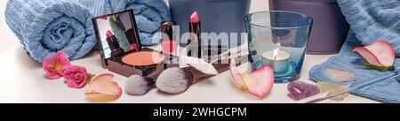 Make-up utensils like face powder, red pink lipstick and nail polish with cosmetic brushes, blue towels, candle and flower petal Stock Photo