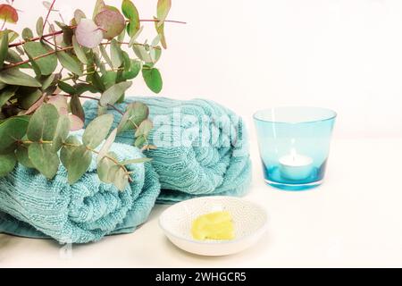 Small bowl with cosmetic moisturizer or emollient for pedicure and soft foot skin, blue towels, candle and some green twigs on a Stock Photo