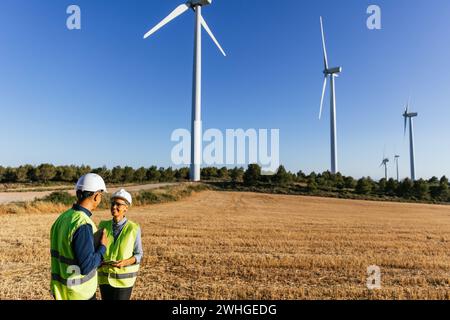 Electrical engineers inspect a wind power plant wearing reflective vests and white helmets. Stock Photo