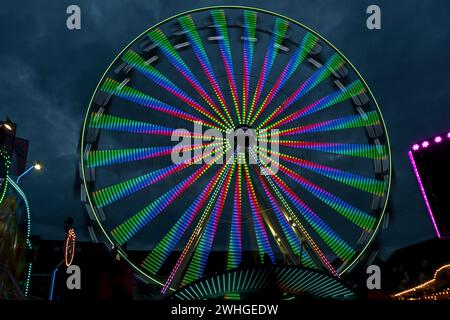 Long exposure of a giant wheel in motion with colorful lights at a christmas fair against a cloudy night sky, abstract image Stock Photo