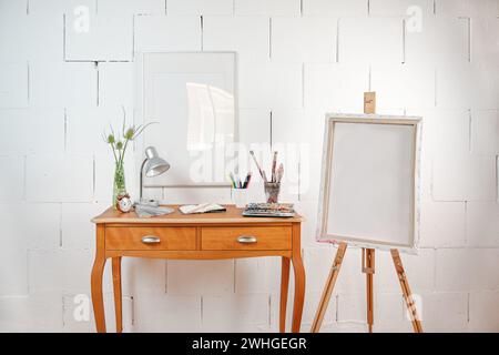 Tiny workplace for creative art work or hobby, crayons, sketchbook, watercolor and brushes on a wooden table and an easel with a Stock Photo