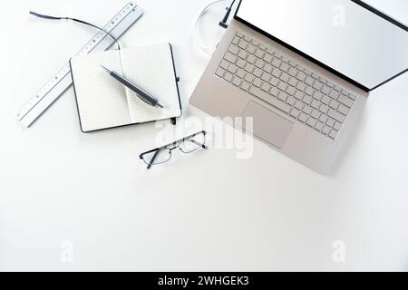 Silver gray laptop with empty screen, notebook, pen and glasses on a white office desk, copy space, high angle view from above Stock Photo