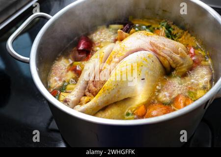 Chicken soup with vegetables and spices is boiling in a pot, cooking a healthy broth, home remedy against cold and flu, selected Stock Photo