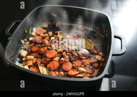 Roasted vegetables for a tasty sauce base in a black cooking pan with carrots, onions, leeks, celery and bay leaves, copy space, Stock Photo