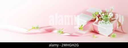 Romantic love gift with ribbon and white flowers on a pink peach background in panoramic format for Valentines day, Mothers day, Stock Photo