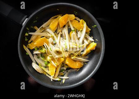 Slices of chicory and orange with spring onions in a black frying pan on the cooker to, vegetarian and vegan meal for a healthy Stock Photo